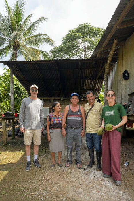 Group of five people standing outdoors in a rural setting with trees and a building in the background.